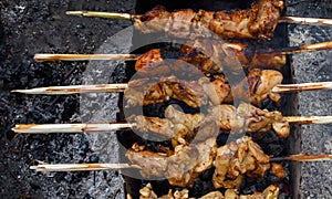 Chicken skewers are fried on ecological wooden skewers. An old iron grill stands on the ground. A lot of gray soot.