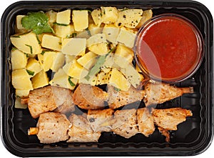 Chicken skewers with potatoes in disposable rectangular plastic black lunch box top view on white background