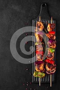 Chicken skewers with slices of sweet peppers and onion. Shish kebab grilled meat on black background. top view