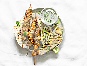 Chicken skewers souvlaki, grilled zucchini, tortillas and tzadziki sauce - delicious greek style lunch on a light background, top