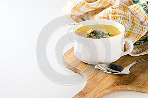 Healthy chicken soup with dill in a white bowl on a wooden cutting board with metal spoon and yellow kitchen towel