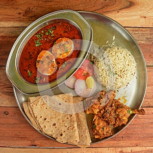 Chicken Thali from an indian cuisine, food platter consists Chicken fry,Boiled egg curry, lentils, jeera rice, and onions.