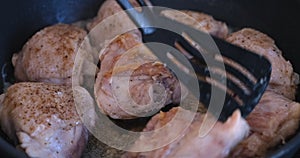 Chicken thighs being flipped over in a frying pan.