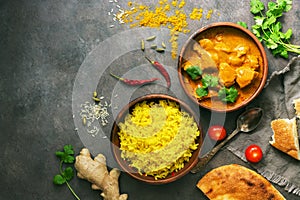 Chicken tikka masala spicy curry meat food in a clay bowl, rice and naan bread . Dark background, top view, place for text