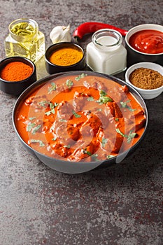 Chicken tikka masala traditional dish of indian cuisine in a black bowl with ingredients over dark concrete background. Vertical