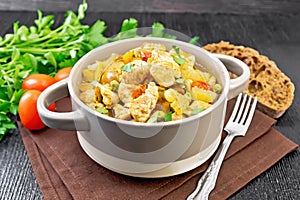 Chicken with vegetables and peas in saucepan on dark board