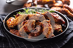 Chicken wings barbeque in a cast iron baking dish with BBQ sauce and rosemary
