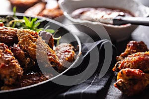 Chicken wings barbeque in a cast iron baking dish with BBQ sauce and rosemary