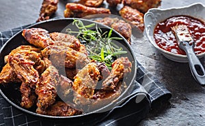 Chicken wings barbeque in a cast iron baking dish with BBQ sauce and rosemary