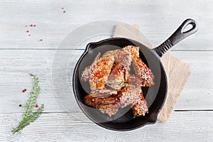 Chicken wings in cast-iron pan. Marinated in tomato and honey sauce. Baked with sesame seeds. Top view, wooden table