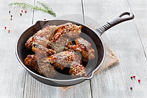 Chicken wings in cast-iron pan on wooden table. Marinated in tomato and honey sauce. Baked with sesame seeds