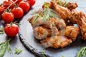 Chicken wings cooked with barbecue sauce on black stone background. Small cherry tomatoes and dill