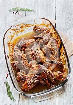 Chicken wings marinated in tomato and honey sauce. Baked with sesame seeds. Baking dish, top view, wooden table