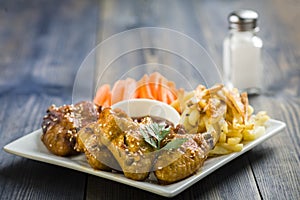 Chicken wings with sesame surrounded by fries and carrots