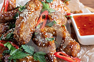 Chicken wings in soy sauce. Served for beer. Sprinkle with sesame seeds. Next to chili pepper sauce and tomatoes. On a wooden