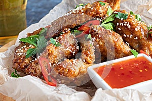 Chicken wings in soy sauce. Served for beer. Sprinkle with sesame seeds. Next to chili pepper sauce and tomatoes. On a wooden