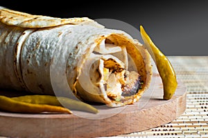 Chicken wrap doner kebap in lavash pita bread durum with thin green pepper pickle on wooden platter