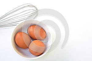 Chickken eggs in a bowl and egg whisks on white background.