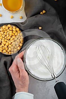 Chickpea aquafaba. Egg replacement. Vegan cooking concept. Men hands whippe whisk chickpeas liquid in glass bowl