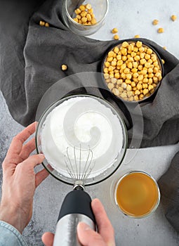 Chickpea aquafaba. Egg replacement. Vegan cooking concept. Men hands whippe whisk chickpeas liquid in glass bowl