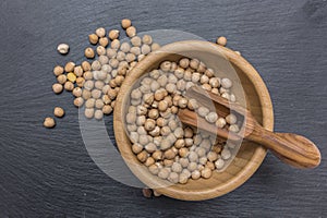 Chickpea and olive wood scoop in a wooden cup on black background of slate or stone