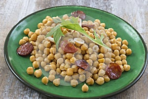 Chickpeas with chorizo on a green plate on wooden table photo