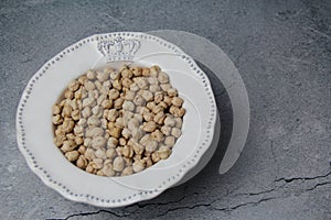 Chickpeas (Cicer arietinum), in a decorated white bowl, on a rustic gray background, top view.