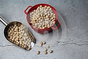 Chickpeas (Cicer arietinum) in a frying pan and a metal measuring spoon on a rustic gray background.