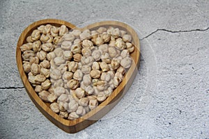 Chickpeas (Cicer arietinum), in a heart-shaped wooden bowl, top view.