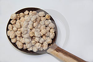 Chickpeas (Cicer arietinum), in a wooden spoon made with coconut shell, isolated on a white background.