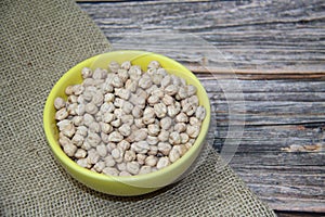 Chickpeas (Cicer arietinum) in a yellow bowl on a jute fabric and a wooden table