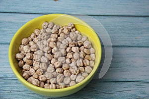 Chickpeas (Cicer arietinum), in a yellow crockery bowl, isolated on wooden table, top view.