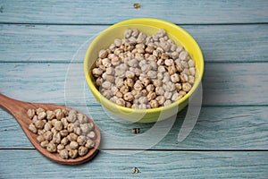 Chickpeas (Cicer arietinum), in a yellow crockery bowl and wooden spoon, isolated on wooden table.