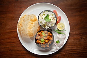 Chickpeas masala Spicy chola or chhole curry and Bhatura or Puri  garnished with fresh green coriander and ingredients.