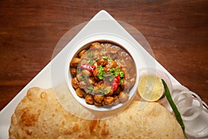 Chickpeas masala Spicy chola or chhole curry and Bhatura or Puri  garnished with fresh green coriander and ingredients.