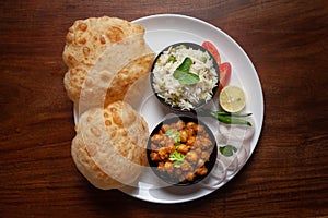 Chickpeas masala Spicy chola or chhole curry and Bhatura or Puri  garnished with fresh green coriander and ingredients.