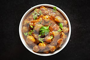 Chickpeas masala Spicy chola or chhole curry  garnished with fresh green coriander and ingredients. Served in a ceramic bowl.