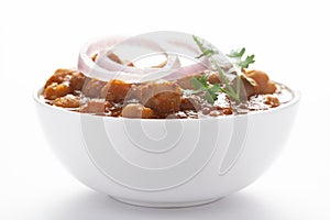 Chickpeas masala Spicy chola or chhole curry  garnished with fresh green coriander and ingredients. Served in a ceramic bowl.