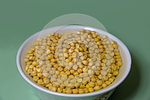 Chickpeas soaked in water in a white deep dish on a green background