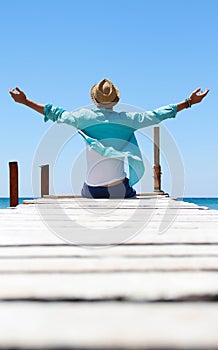 boy sitting on pier with hat in front of the sea photo