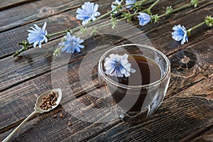 Chicory drink in thermo glass cup with instant granules in spoon on wooden table