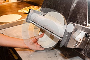 Chief cook rolls the dough for pizza with special equipment