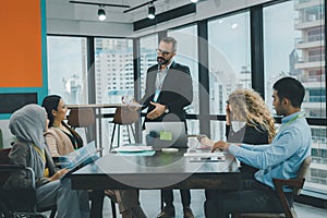 Chief executive male officer is standing at the head of the desk to introduce the new project. Group of employee are sitting and