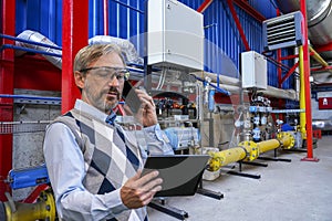 Chief Executive Officer Looking At Digital Tablet Screen And Talking On Smart Phone In Industrial Interior