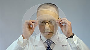 Chief physician putting on glasses, ready to examine patient, looking at camera