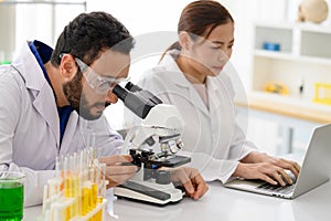 Chief research scientist adjusts specimen in petri dish and looks into microscope