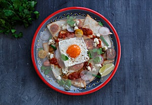 Chilaquiles Mexican tortilla with tomato salsa, chicken and egg close-up on a plate. Horizontal view from above