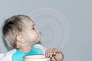 A child 1-2 years old eats. Portrait of a happy toddler boy with spoon at the kitchen table.