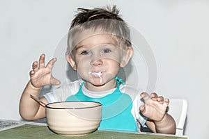 A child 1-2 years old eats. Portrait of a happy toddler boy with spoon at the kitchen table.