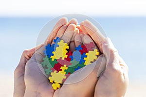 Child and adult hands holding colorful heart with blue background outdoors. World autism awareness day concept